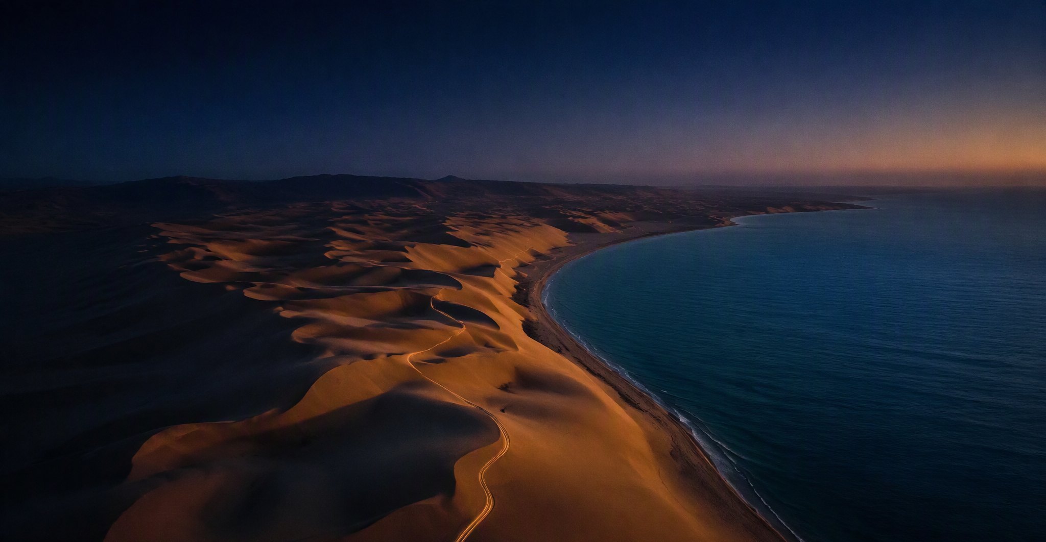 كثبان الصحراء تلتقي بالبحر عند الغسق